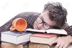Exhausted young male Caucasian student with glasses asleep on pile of books next to spilled cup of coffee on white background with copy text space